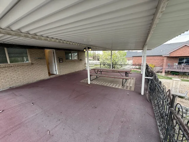 Covered outdoor patio with a corrugated roof, brick exterior, and wrought iron railing
