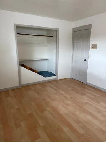 Wood-finish flooring, white painted walls, and a built-in closet with shelving and a hanging rod. Photo shown was taken prior to tenant occupancy and is provided for reference.