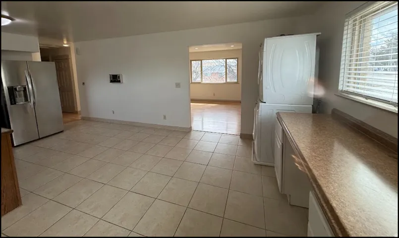 Expansive tiled flooring, ample cabinetry, and a stacked laundry appliance area. Photo shown was taken prior to tenant occupancy and is provided for reference.