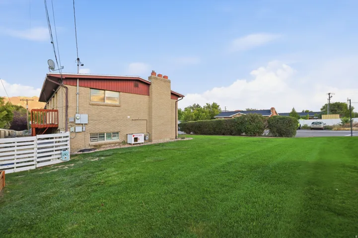 Expansive lawn area with a brick exterior, upper-level wood deck, and a privacy fence