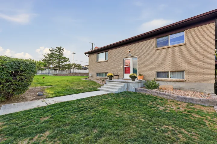 Brick exterior with a concrete patio and steps, complemented by a manicured lawn and established shrubbery