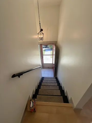 Foyer featuring a contemporary hanging lantern, a full-lite entry door, and staircase with a dark handrail. Photo shown was taken prior to tenant occupancy and is provided for reference.