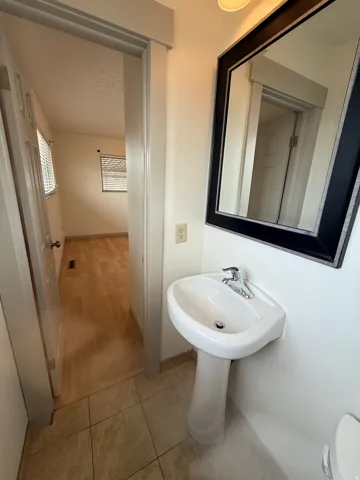 Pedestal sink with chrome faucet, large framed mirror, and tile flooring. Photo shown was taken prior to tenant occupancy and is provided for reference.