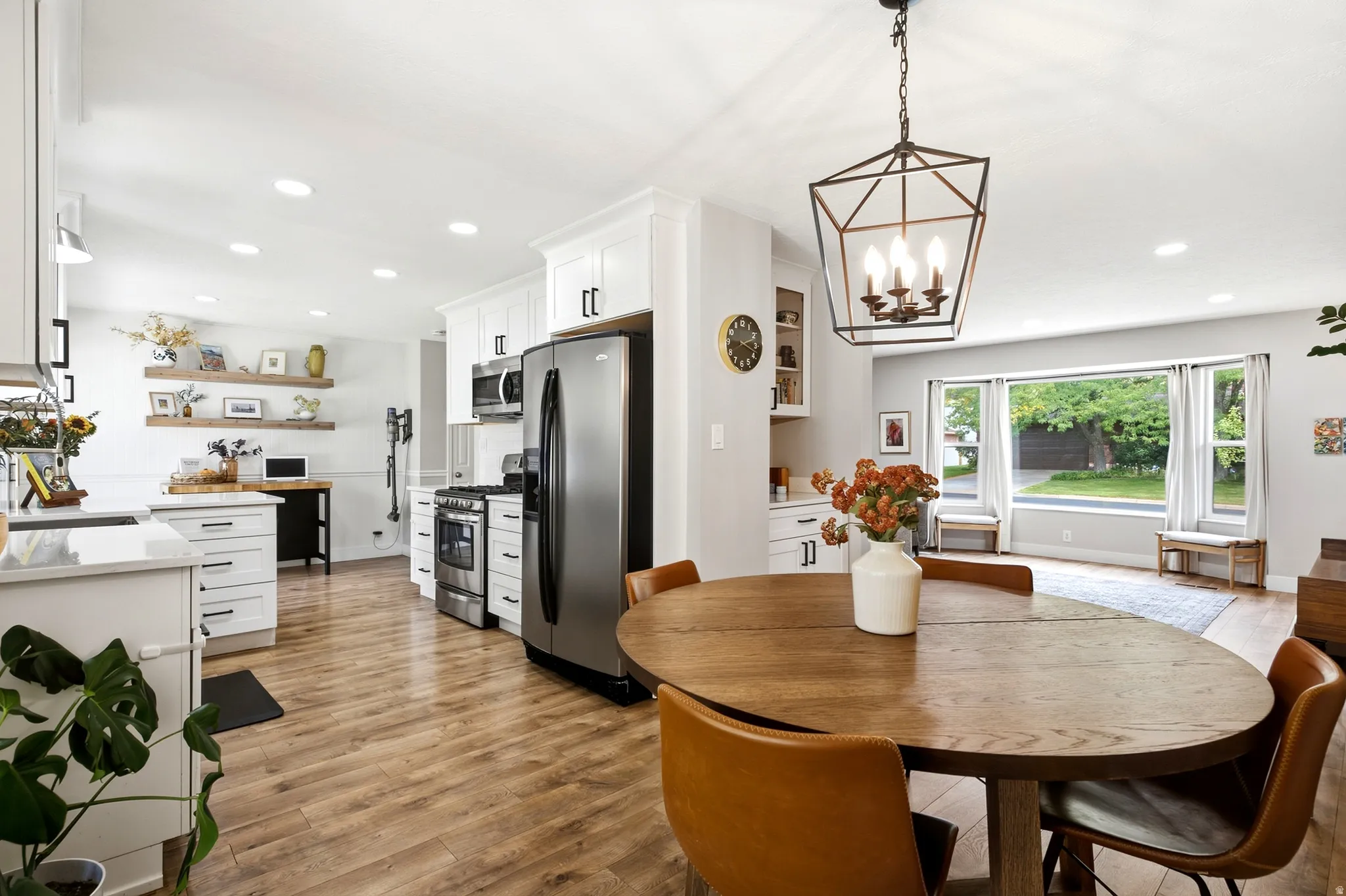 Expansive kitchen featuring white cabinetry, stainless steel appliances, wood-finish flooring, recessed lighting, and a contemporary geometric chandelier