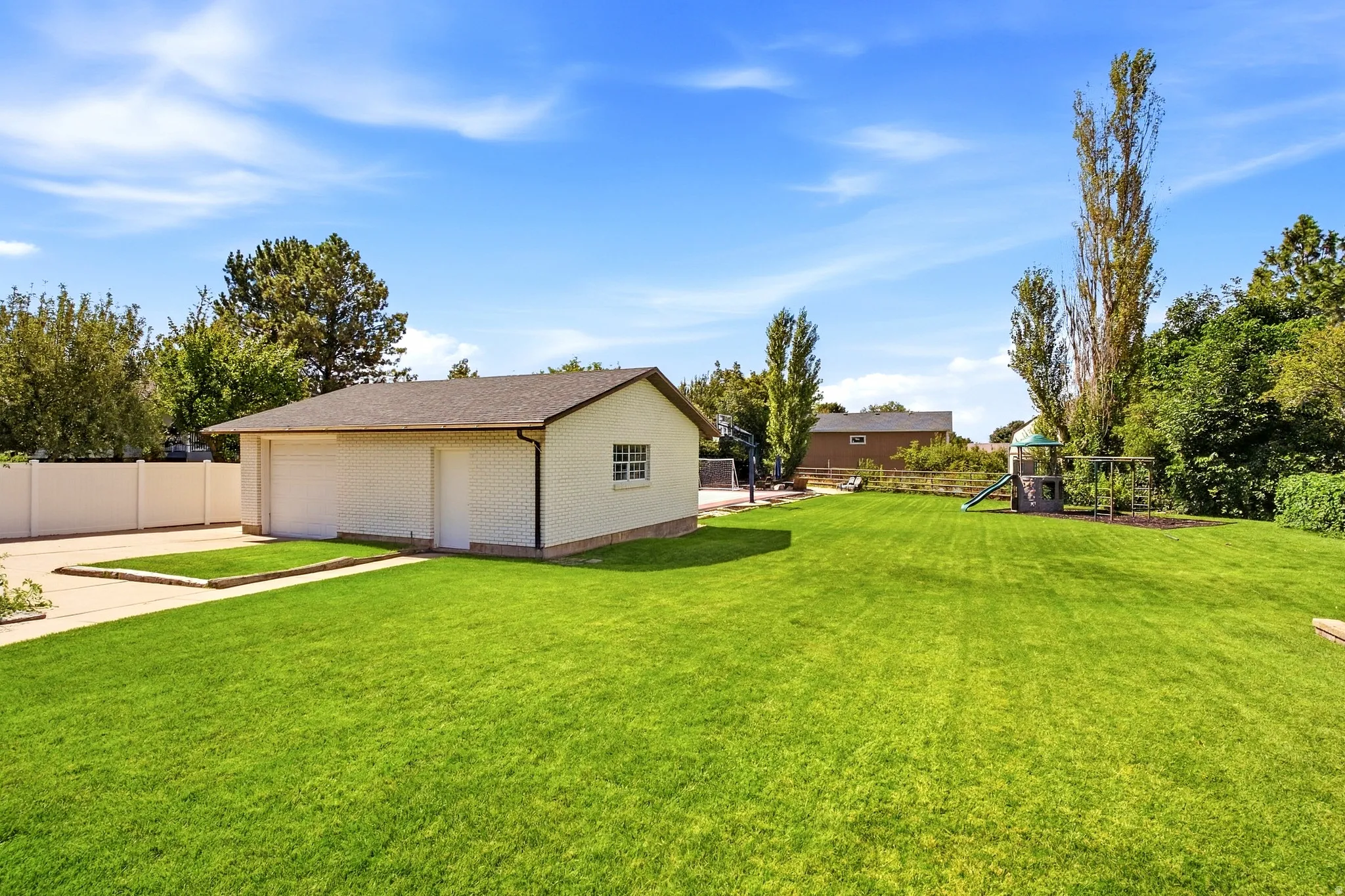 Expansive lawn area with a detached garage building, concrete driveway, and white privacy fencing