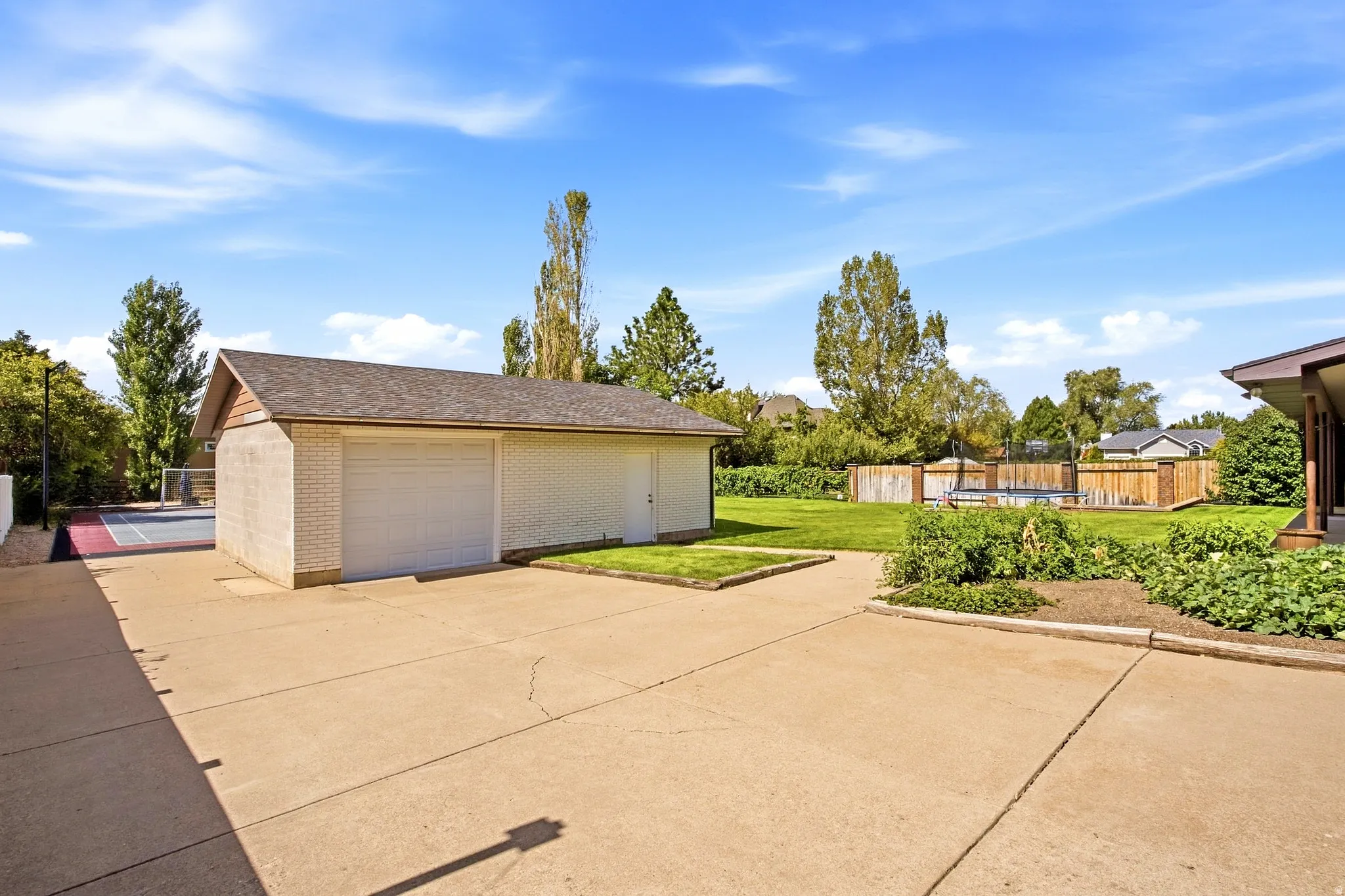 Detached garage with dual overhead doors, expansive concrete driveway, fenced yard, and dedicated court space