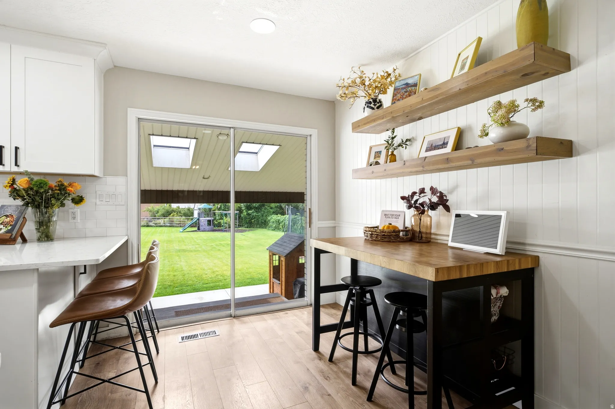 White shaker cabinetry with dark hardware, wood-finish flooring, white subway tile backsplash, and a sliding glass door