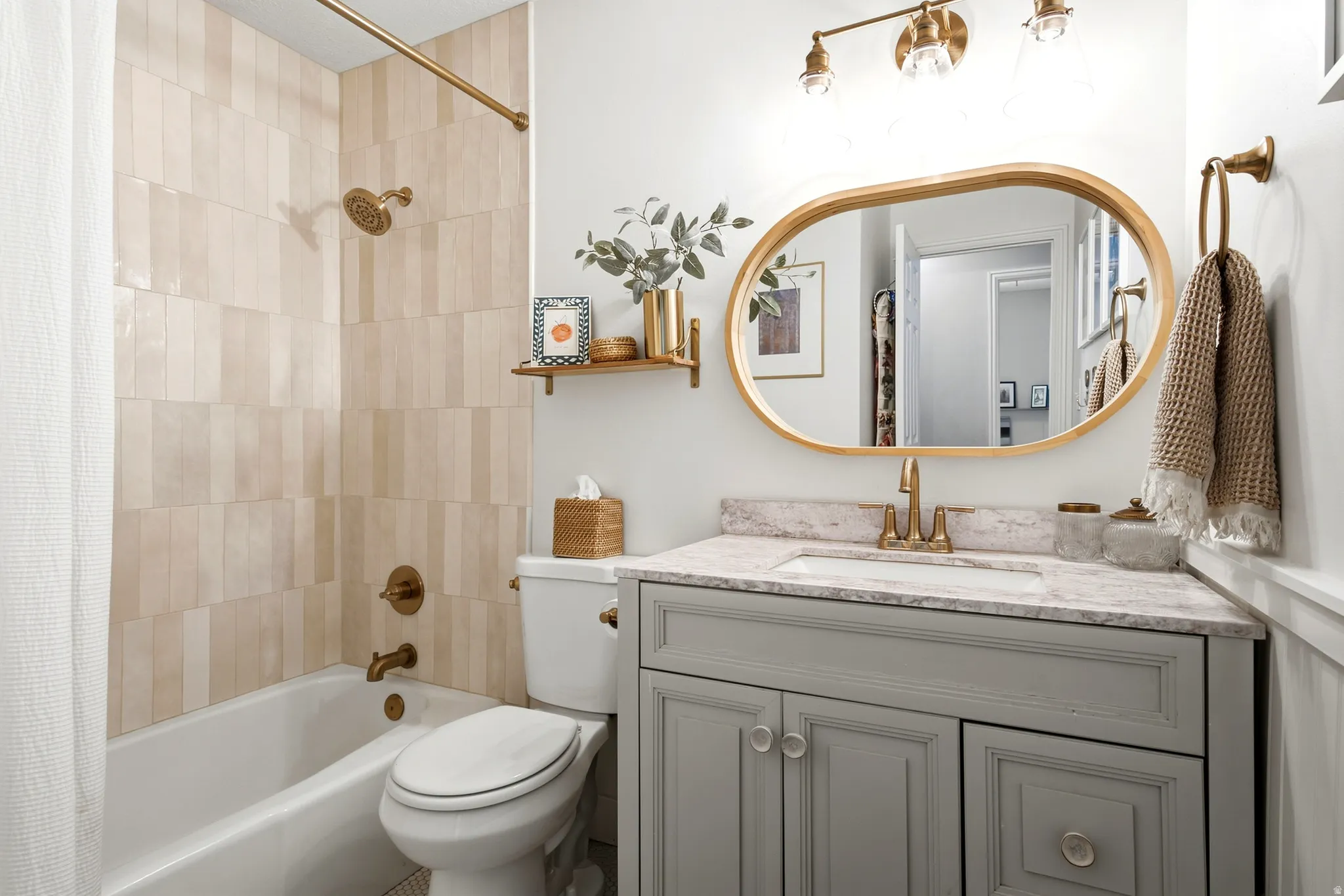 White soaking tub with shower, vertical tile shower surround, single vanity with light gray cabinetry, built-in sink, and stone-finish countertop