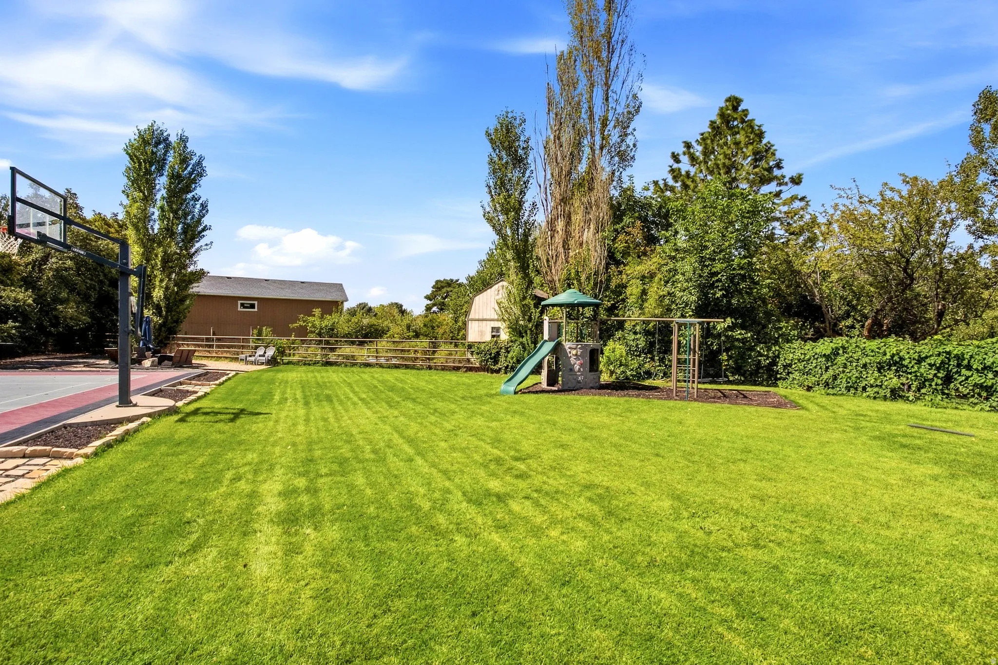 Expansive lawn with a built-in playset, swing set, and a sports court featuring a basketball hoop