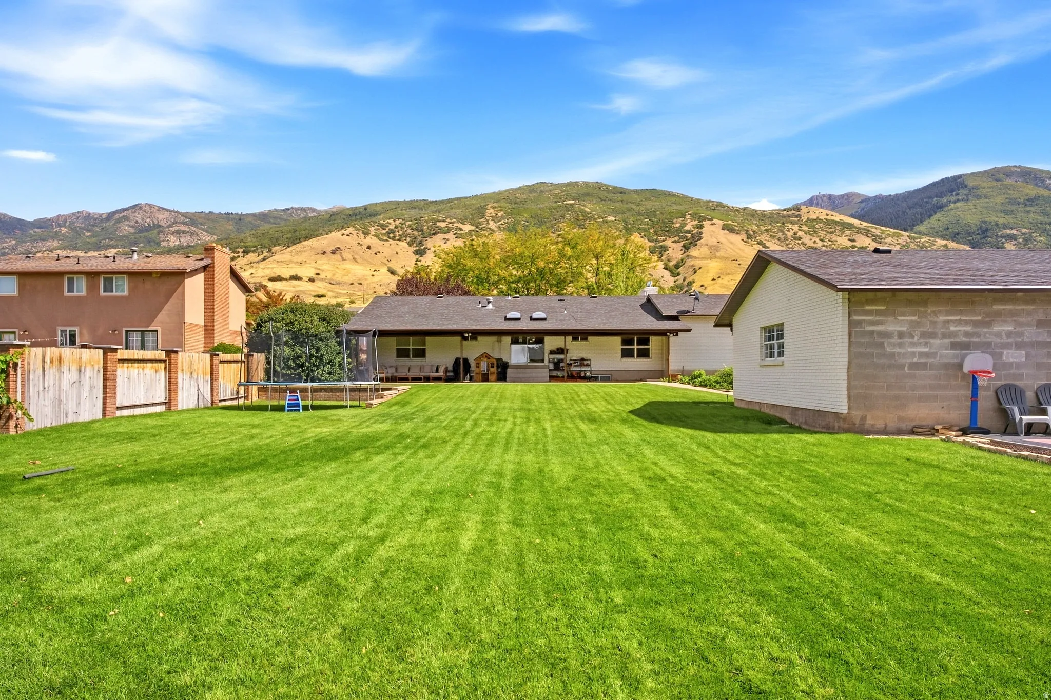 Expansive green lawn with mountain backdrop, featuring a covered patio, and a detached building with block construction