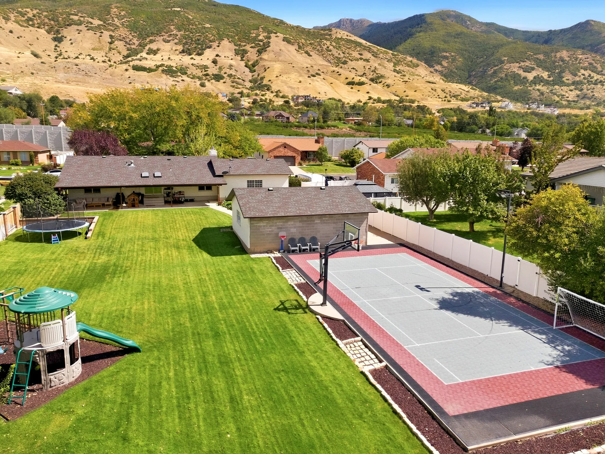 Expansive backyard featuring a manicured lawn, a hardscaped sports court, and a detached storage structure