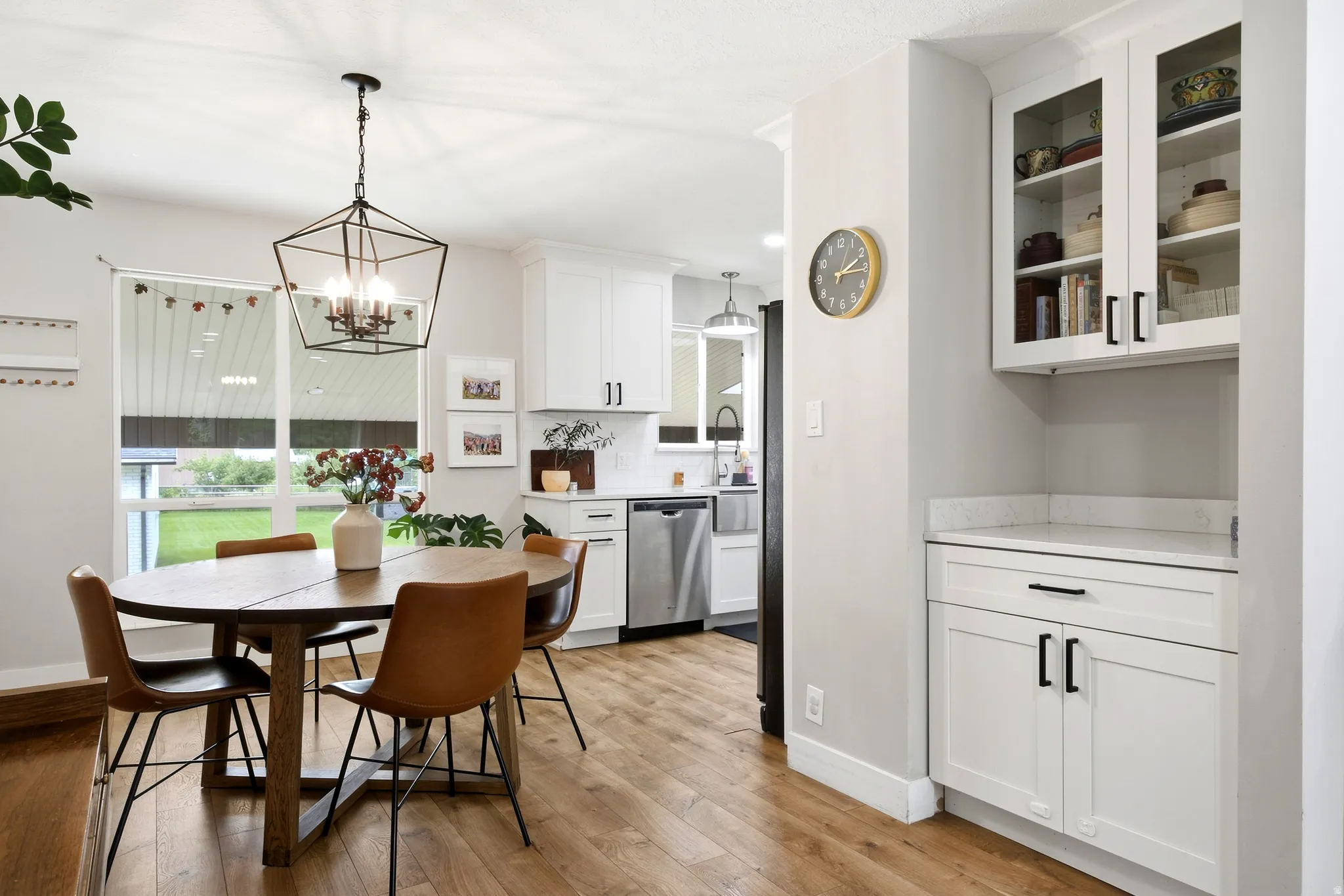Wood-finish flooring, white cabinetry with black hardware, stainless steel dishwasher, and a geometric pendant light fixture