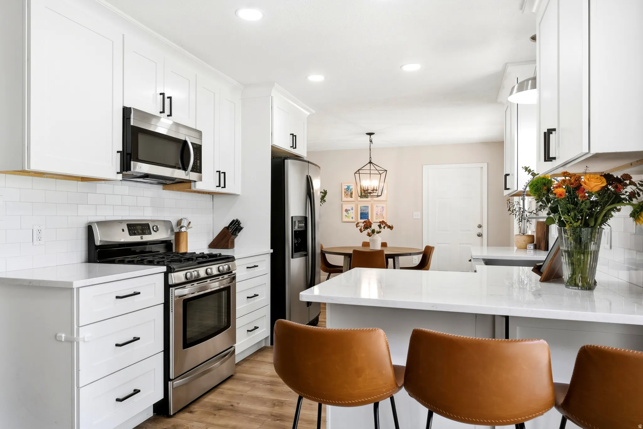 Updated kitchen featuring white shaker cabinetry, stainless steel appliances, white subway tile backsplash, white countertops, and wood-finish flooring