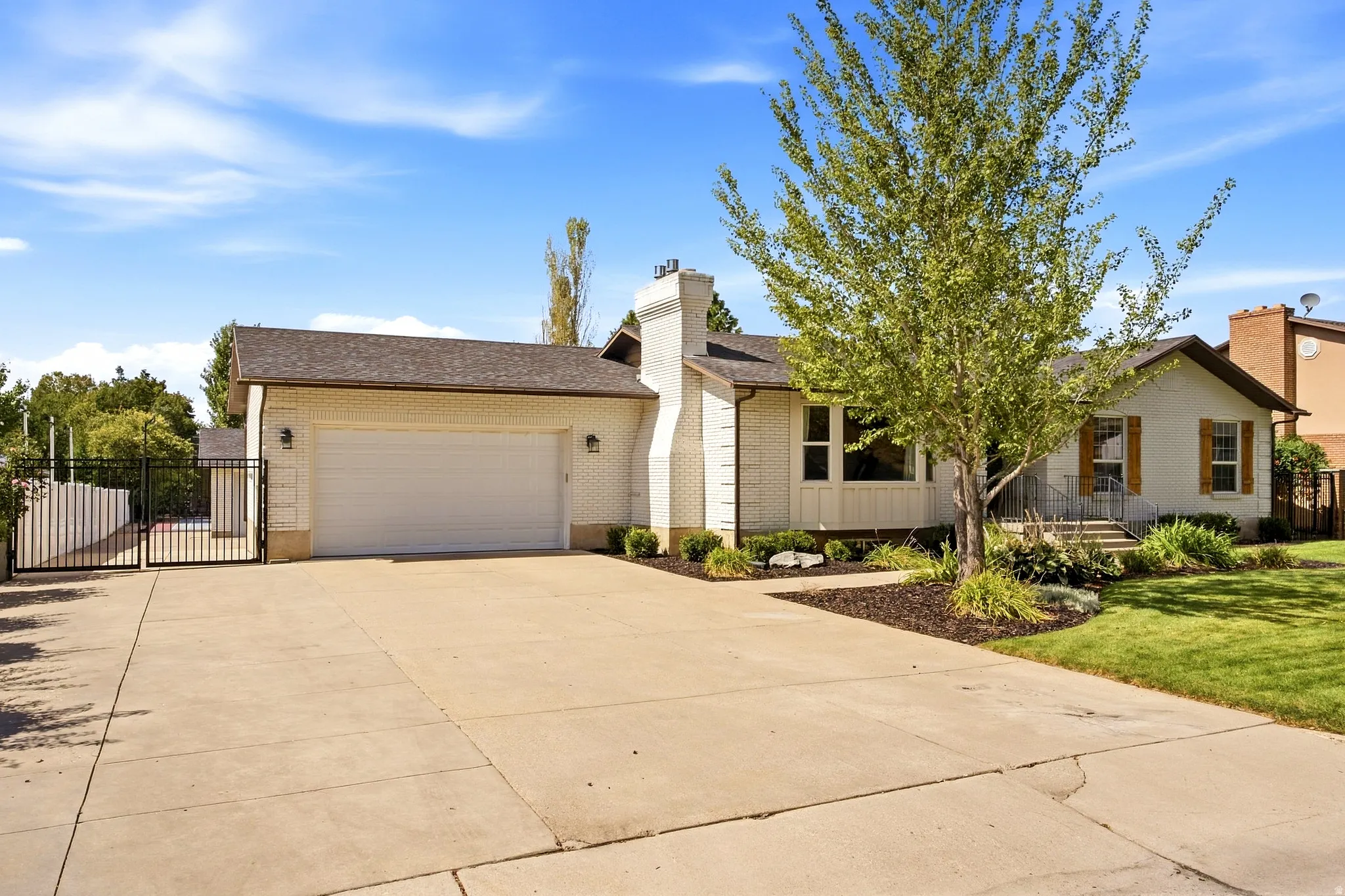 White brick facade with brown roof, attached garage, and mature tree