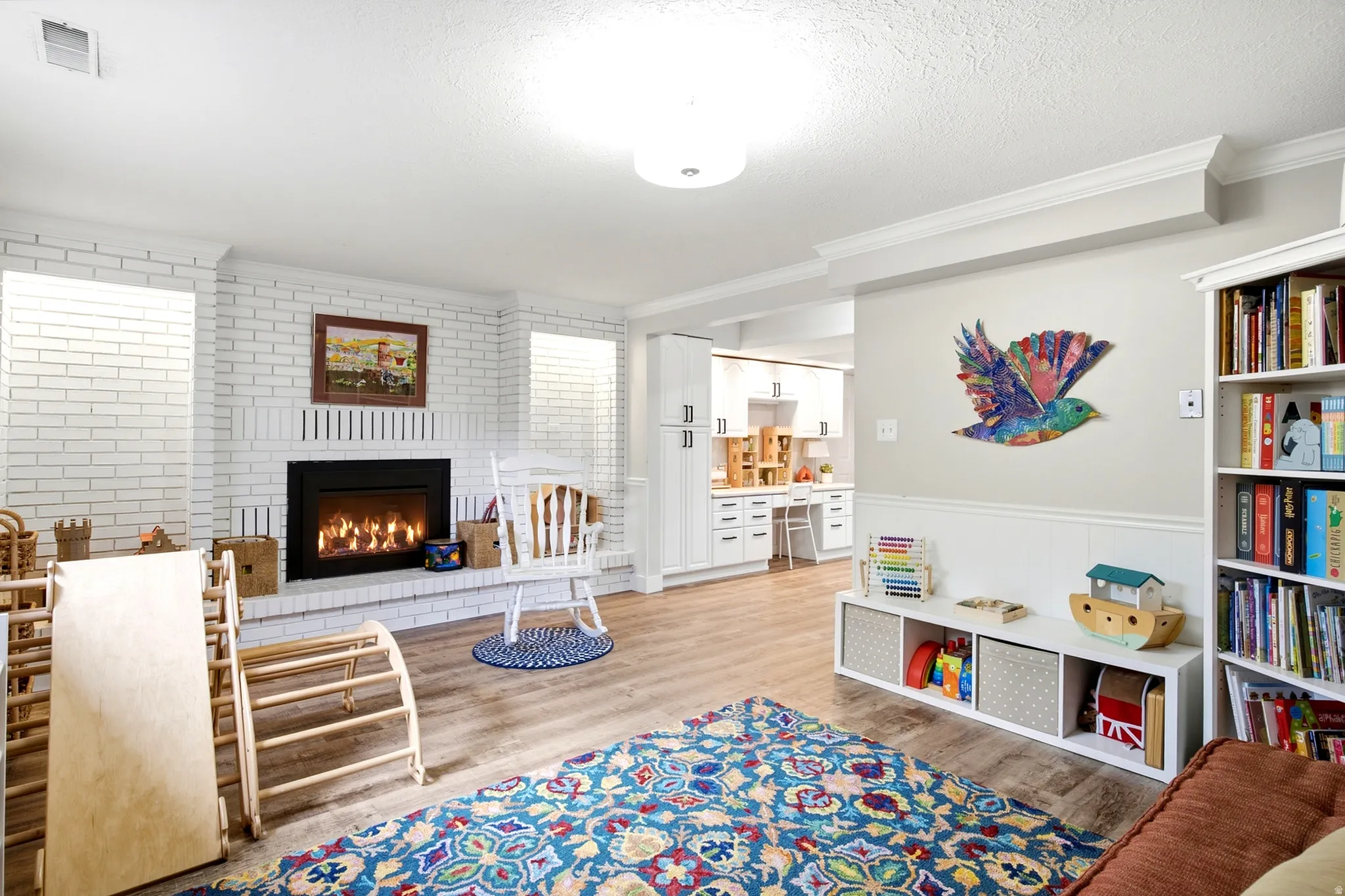 White brick fireplace with an integrated firebox, wood-finish flooring, built-in shelving, and white wainscoting