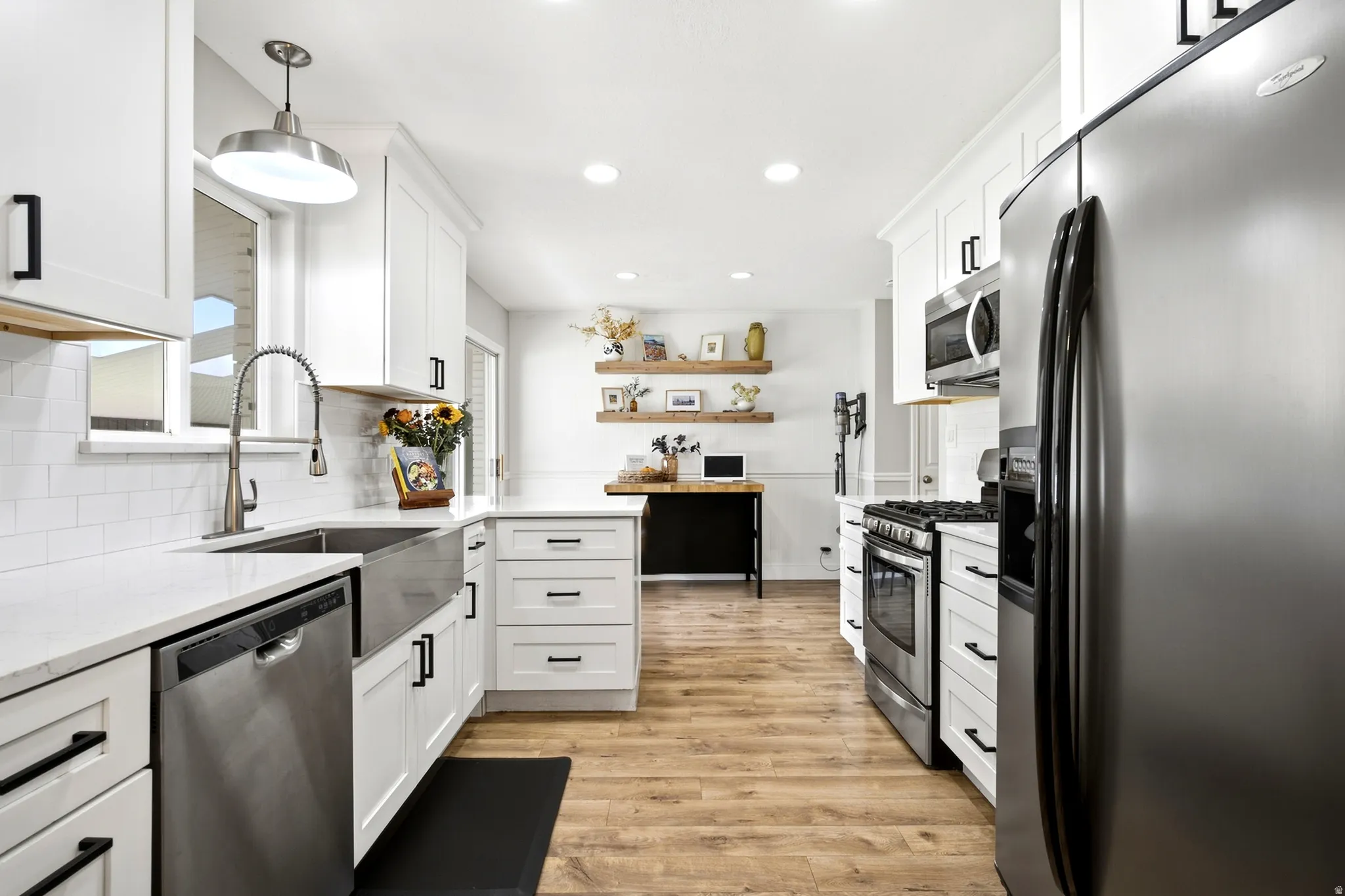 White shaker-style cabinetry with black hardware, stainless steel appliances, wood-finish flooring, a farmhouse sink, and a white subway tile backsplash