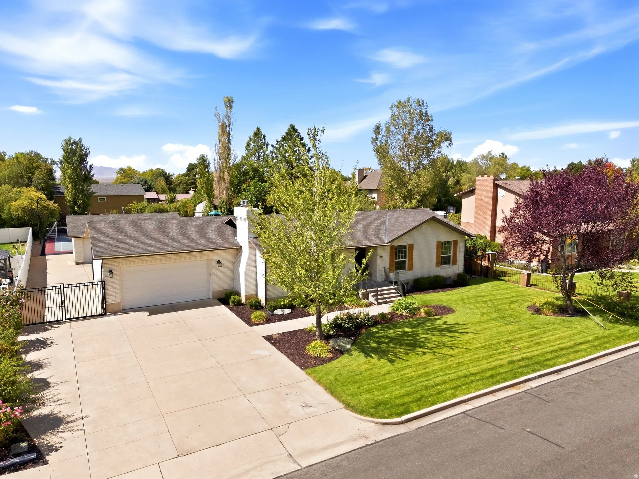 Single-story residence with a two-car garage, mature landscaping, and an expansive concrete driveway