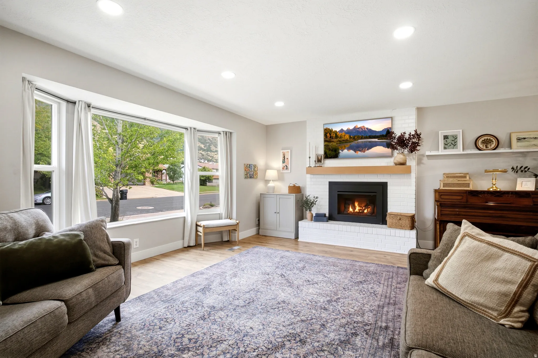 Bay window with multiple panes, recessed lighting, wood-finish flooring, white brick fireplace surround, and a wood mantel