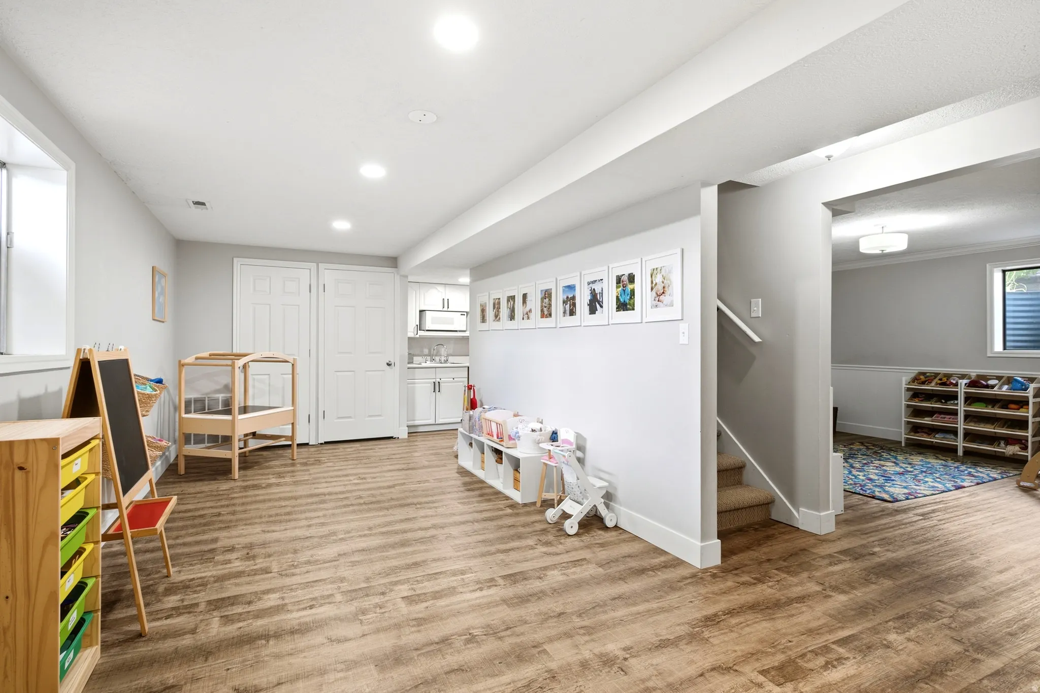 Recessed lighting, wood-finish flooring, white trim, and a built-in wet bar with white cabinetry and a microwave
