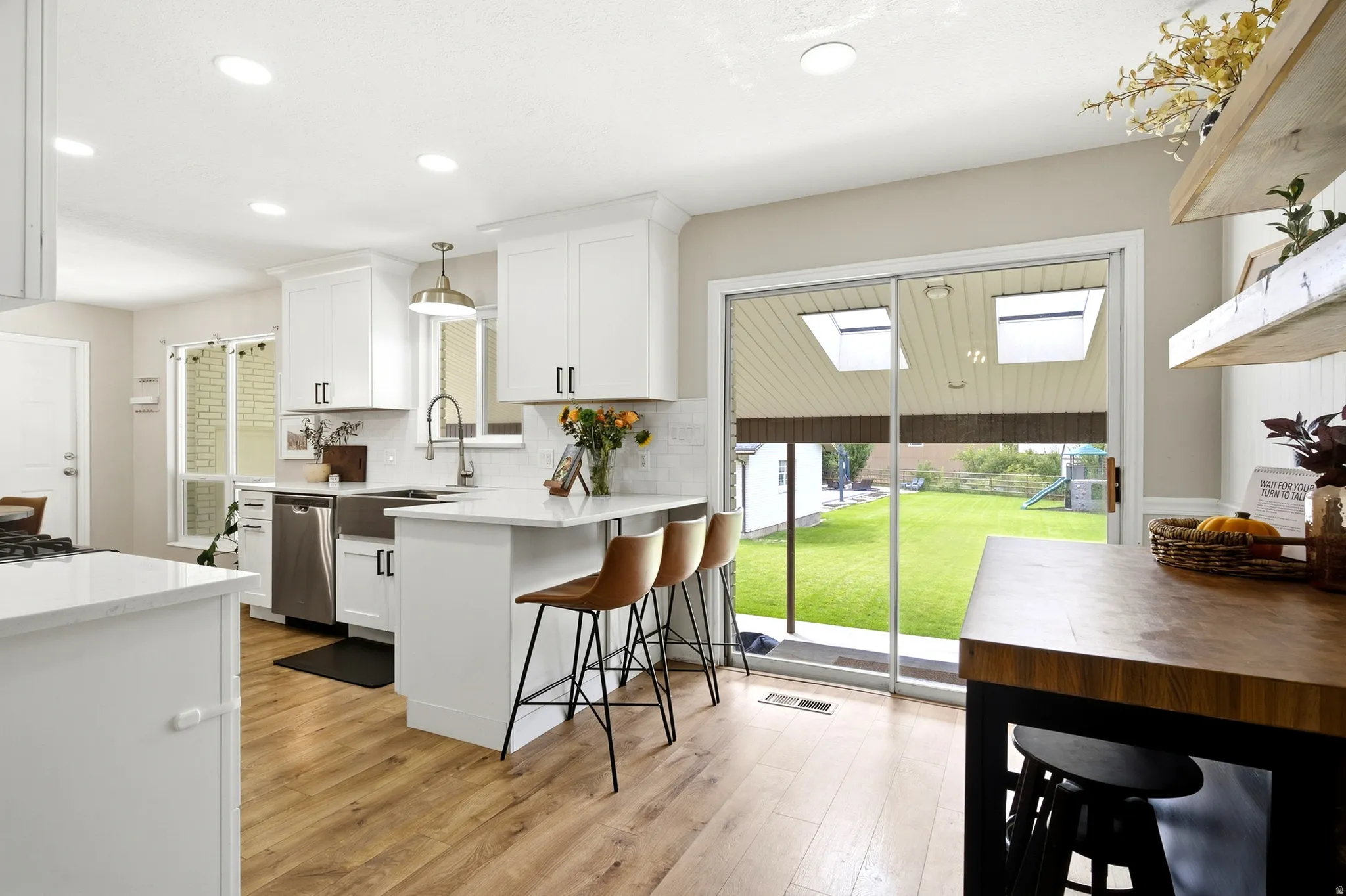 Modern kitchen featuring white cabinetry, stainless steel appliances, wood-finish flooring, and a sliding glass door to the backyard