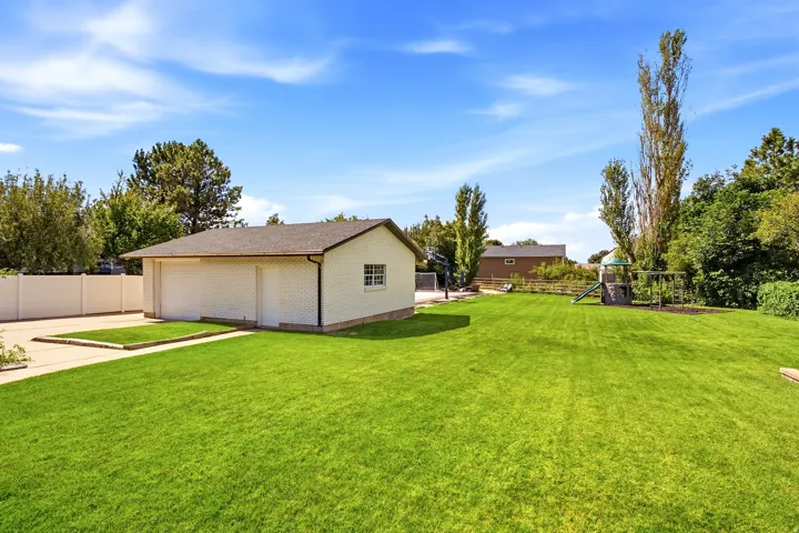 Expansive lawn area with a detached garage building, concrete driveway, and white privacy fencing