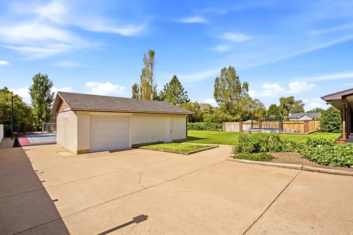 Detached garage with dual overhead doors, expansive concrete driveway, fenced yard, and dedicated court space
