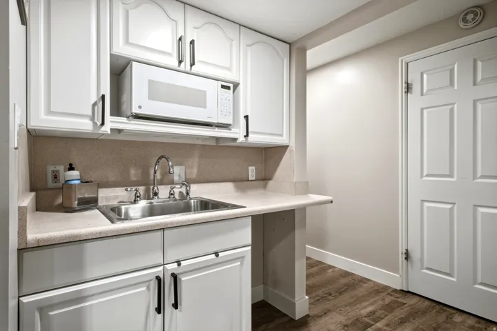 White cabinetry with black hardware, stainless steel sink with chrome faucet, built-in microwave, wood-finish flooring, and a six-panel interior door