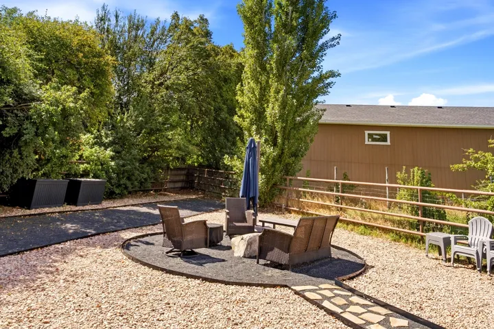 Expansive outdoor space featuring a large gravel area, a defined fire pit zone with dark ground cover, a stone pathway, and mature trees providing natural screening