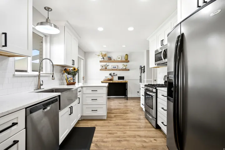 White shaker-style cabinetry with black hardware, stainless steel appliances, wood-finish flooring, a farmhouse sink, and a white subway tile backsplash
