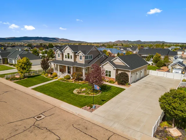 Expansive concrete driveway, attached three-car garage, manicured front lawn, established landscaping, and a covered front porch