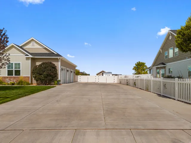 Expansive concrete driveway with a three-car garage and a white privacy fence