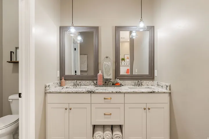 Dual vanity with light-toned cabinetry, speckled countertops, and individual framed mirrors