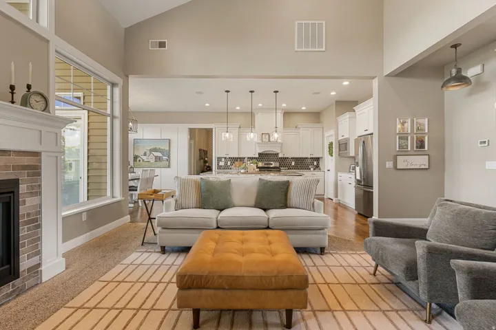 Vaulted ceiling with an accent window, fireplace with a brick surround and white mantel, recessed lighting, white cabinetry, and stainless steel appliances