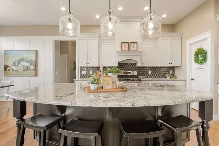 Expansive kitchen island with a stone countertop, white shaker cabinetry, hexagonal tile backsplash, and stainless steel appliances