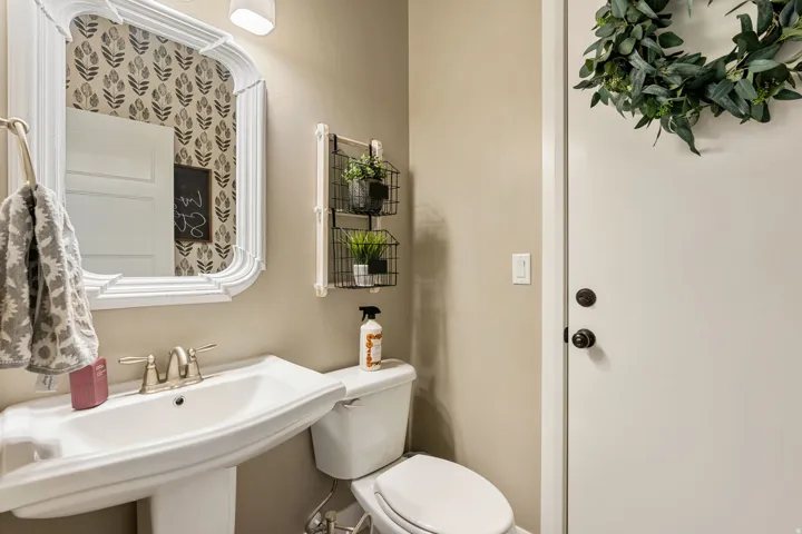 Pedestal sink with a two-handle faucet, wall-mounted mirror, and decorative wallpaper accent