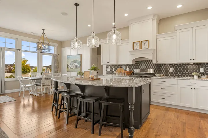 Hardwood-finish flooring throughout, featuring a kitchen island with granite countertop, white cabinetry, dark hexagonal tile backsplash, and large windows
