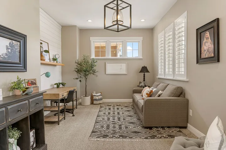 Window shutters, recessed lighting, and a linear chandelier illuminate this space featuring a built-in desk with shelving and a shiplap accent wall