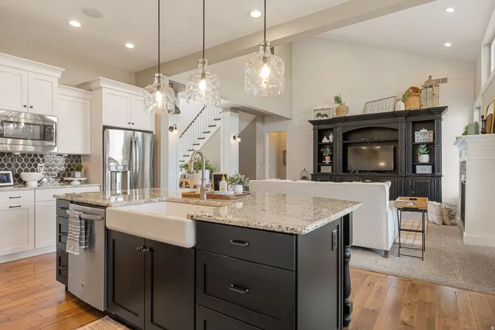 Open-concept kitchen featuring an island with a farmhouse sink, stainless steel appliances, and granite countertops