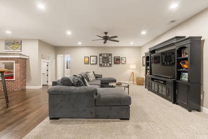 Recessed lighting illuminates this space featuring a ceiling fan, a built-in media console, and a partial brick-finish wall element