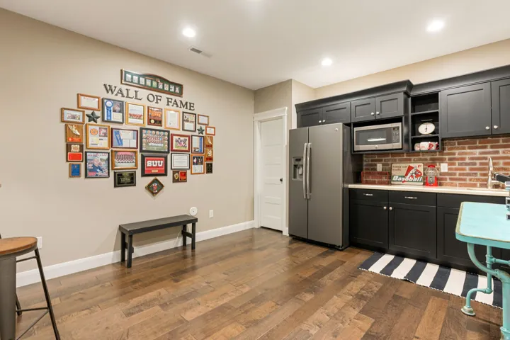 Wood-finish flooring throughout, recessed lighting, built-in black cabinetry, brick-finish backsplash, and a stainless steel refrigerator