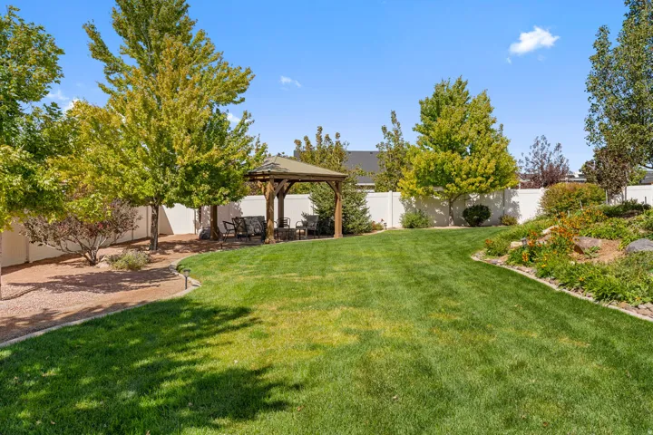 Expansive backyard featuring a lush lawn, mature trees, a privacy fence, and a built-in gazebo
