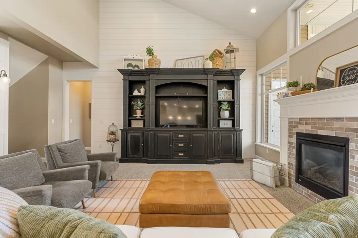 Vaulted ceiling with shiplap accent wall, built-in media center, tile-surround fireplace with mantel, and large windows