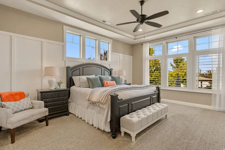 Tray ceiling with recessed lighting and a ceiling fan, broad windows, plantation shutters, and board and batten wall detailing