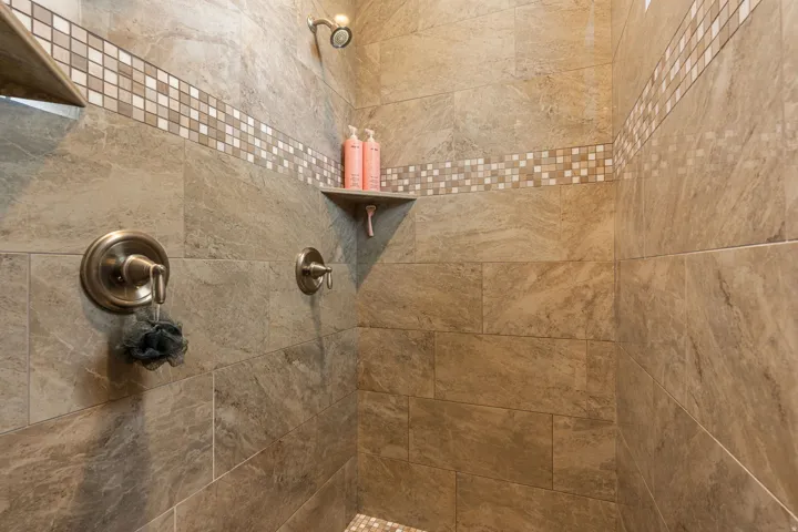 Tiled shower enclosure featuring a mosaic accent band, built-in shelving, and bronze-finish fixtures
