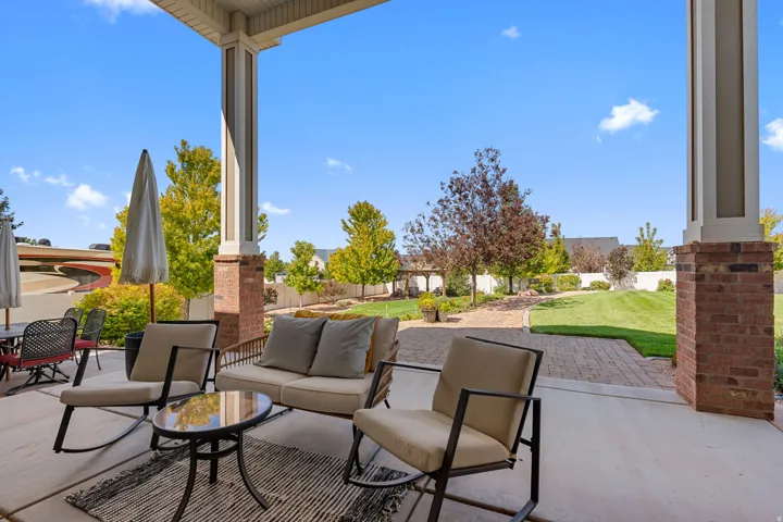 Covered patio with brick columns, concrete flooring, paver walkway, and a manicured lawn