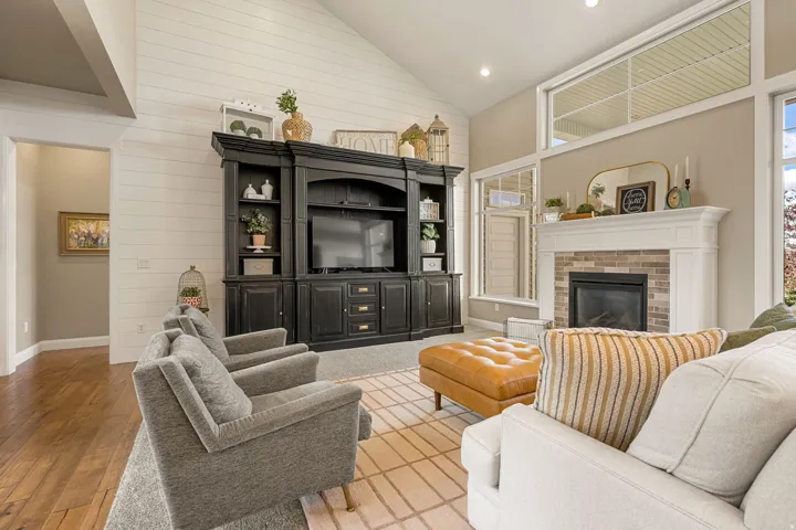 Vaulted ceilings, wood-finish flooring, white shiplap accent wall, fireplace with brick surround and white mantel, and transom windows
