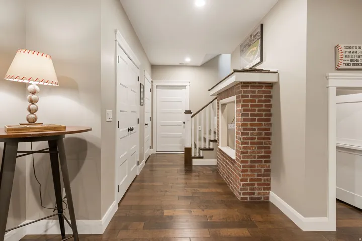 Hardwood-finish flooring, white panel doors, recessed lighting, brick-finish accent wall with window opening, and white painted staircase with wood handrail