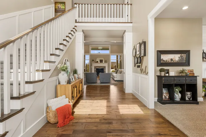 Hardwood-style flooring, white wainscoting, staircase with white risers and wood-finish treads, and an upper-level railing overlooking the entry