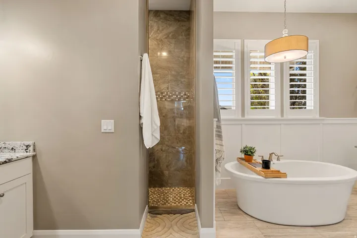 Recessed shower with tiled surround and mosaic accent, freestanding bathtub, shuttered windows, and board and batten wall detailing