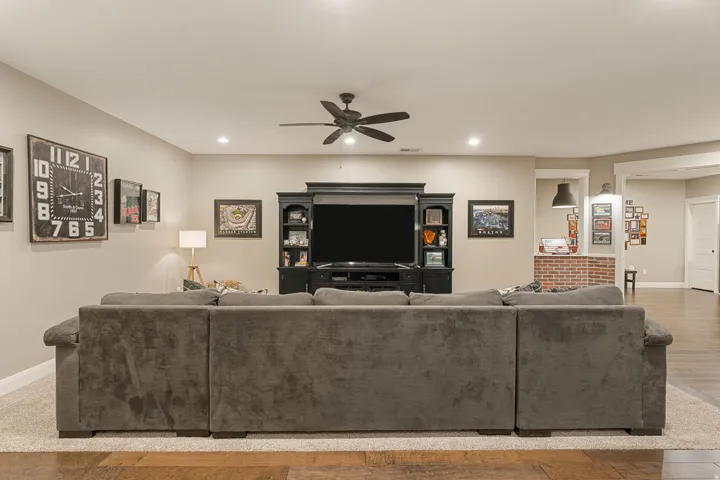 Recessed lighting, ceiling fan, built-in entertainment center, brick accent wall, and wood-finish flooring